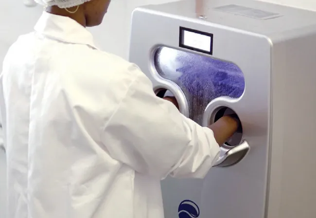 A staff member in a hairnet and lab coat using the Scrubzone automated hand hygiene machine